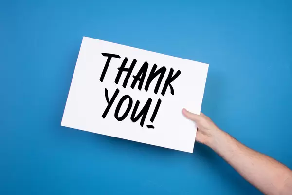 Hand holding white banner with Thank you text on blue background