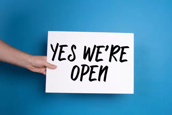 Hand holding white banner with Yes We're open text on blue background