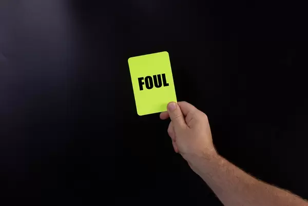 Hand holding yellow referee card with Foul text on black background