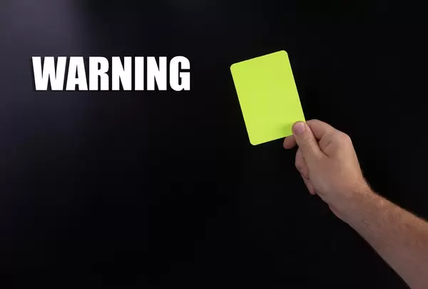 Hand holding yellow referee card with Warning text on black background