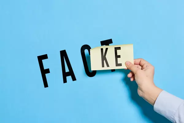 Hand holds a piece of paper with text fake over fact text. Fake or Fact concepts