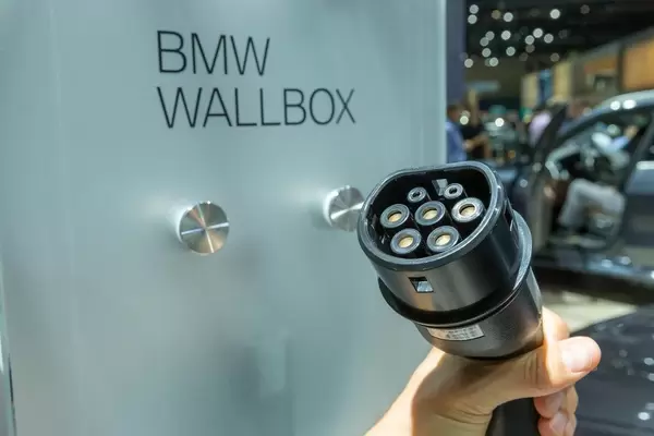 Hand holds a portable BMW i3 type-2 charger in front of BMW Wallbox