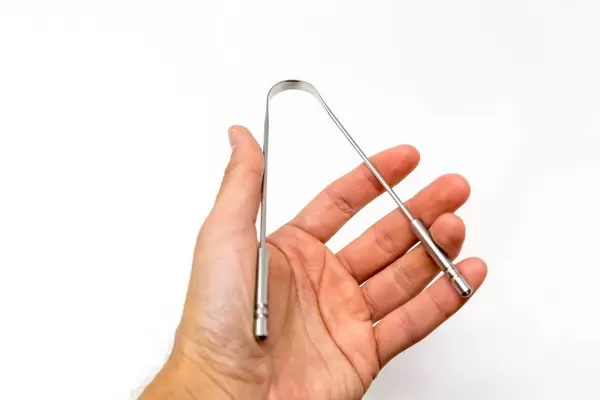 Hand holds a stainless steel tongue scraper from YogaMedic