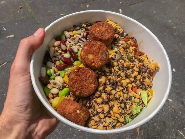 Hand holds a veggie salad mix in a green to-go salad bowl by PicaDeli