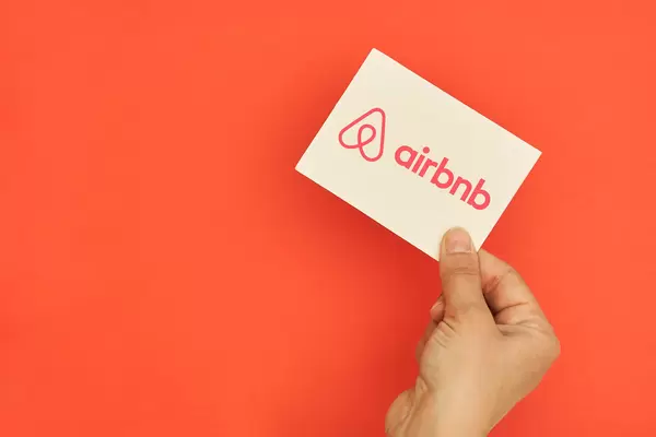 Hand holds Airbnb logotype card over red background