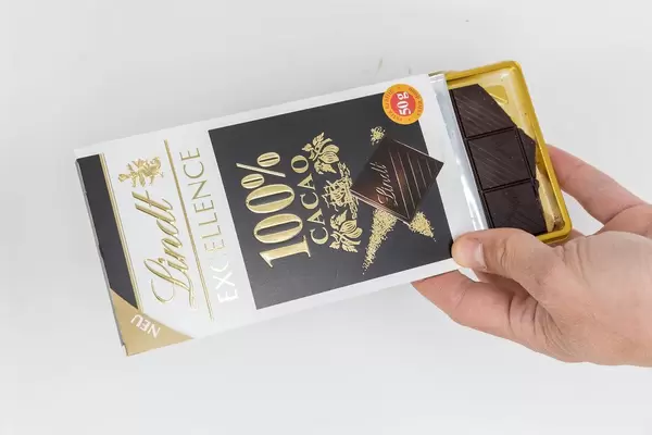 Hand holds an open package of chocolate with 100% cacao by Lindt Excellence with white background