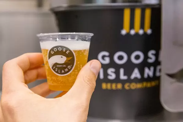 Hand holds beer in a small plastic cup with the brand logo of the famous Chicago Goose Island Beer Company