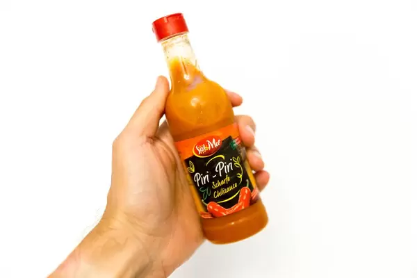 Hand holds hot chili sauce Piri-Piri by Sol&Mar, with white background