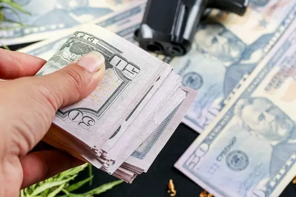 Hand holds money on the background of a gun and dollars