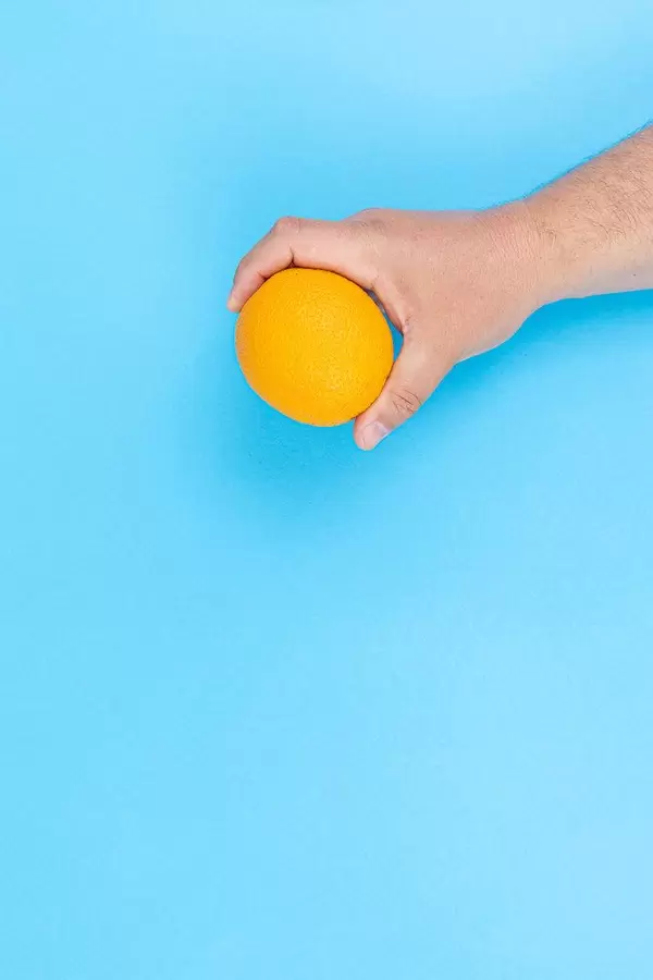Hand holds Orange fruit above blue background