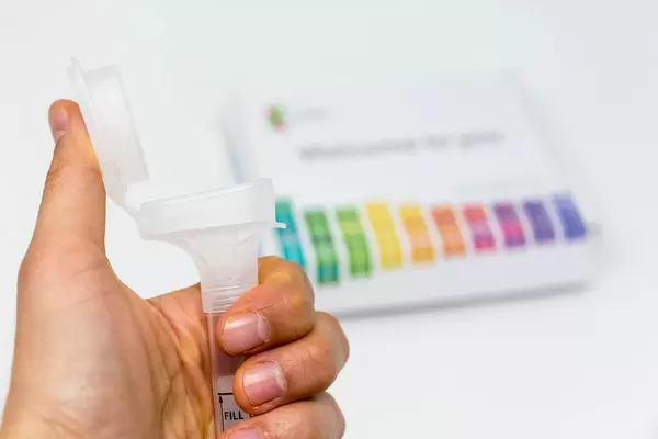 Hand holds Saliva Collection Kit Tube from 23andMe with open funnel lid to test health and ancestry with personal genetic in front of blurry background