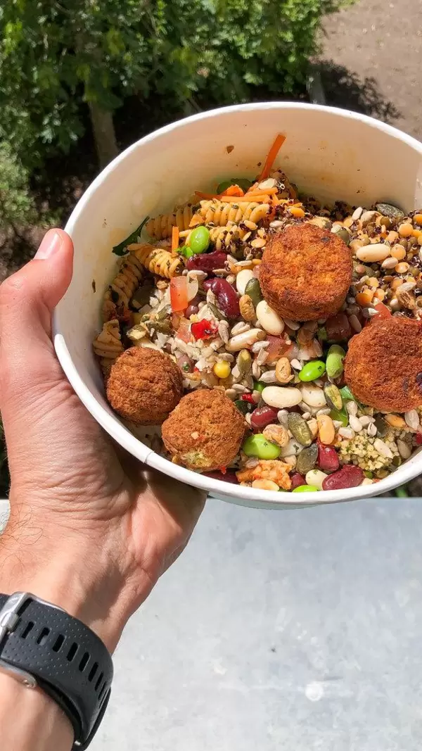 Hand holds self mixed food by PicaDeli salad bar: Powerkorn mix with pasta & vegetarian tomato-basil vegetable balls, in a to-go bowl