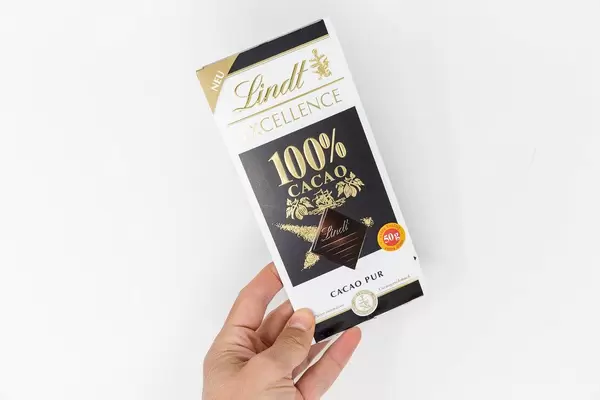 Hand holds the new Lindt Excellence chocolate bar with 100% pure cacao on a white background