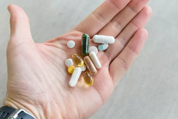 Hand holds various tablets and vitamin pills in front of gray background