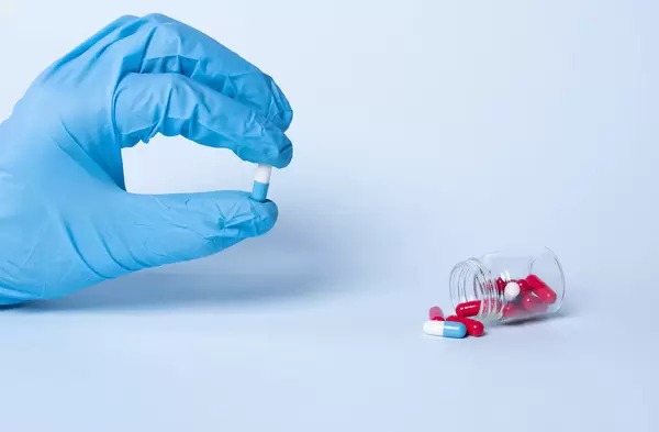 Hand in blue medical gloves holding a pill
