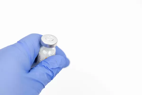 Hand in blue Medical Gloves holds vaccine in glass bottle