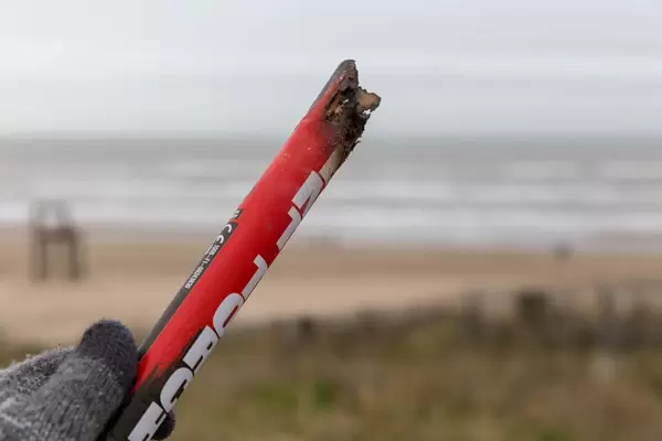 Hand in glove holds charred remains of firework rocket, in the background beach of Zandvoort