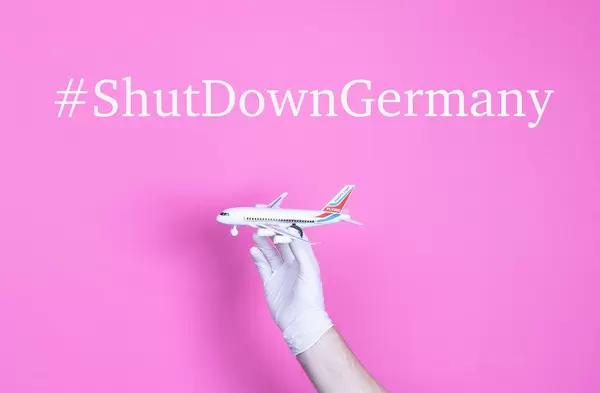 Hand in medical glove holding small airplane with #ShutDownGermany text