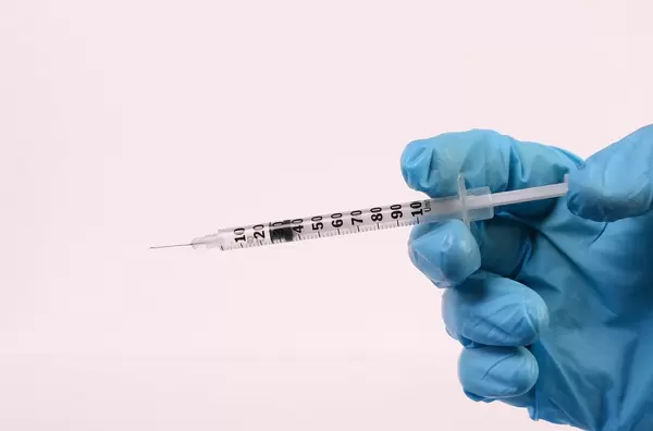 Hand in medical glove with syringe on white background