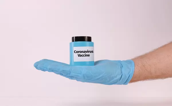 Hand in medical gloves holding bottle with blue fluid and Coronavirus Vaccine text