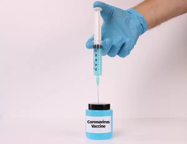 Hand in medical gloves holding syringe over bottle with Coronavirus Vaccine text