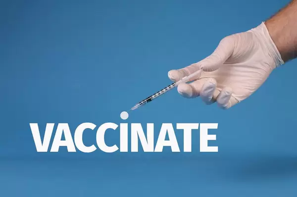 Hand in medical gloves holding syringe over Vaccinate text
