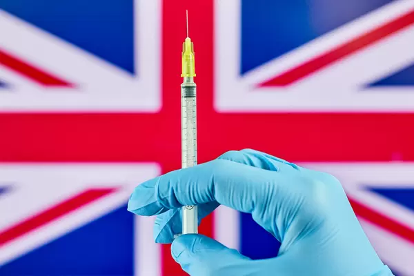 Hand in medical gloves holds syringe with vaccine over the Great Britain flag