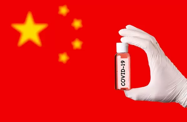 Hand in protective gloves holding COVID-19 test tube in front of flag of China