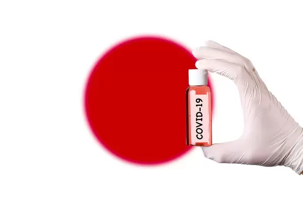 Hand in protective gloves holding COVID-19 test tube in front of flag of Japan