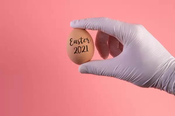 Hand in protective gloves holding egg with Easter 2021 text