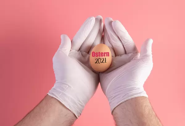 Hand in protective gloves holding egg with Ostern 2021 text