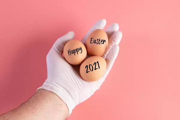 Hand in protective gloves holding eggs with Happy Easter 2021 text