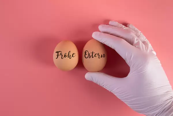 Hand in protective gloves with two eggs and Frohe Ostern text