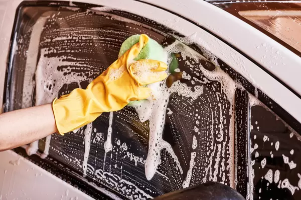 Hand in rubber gloves washing car window with a foamy sponge