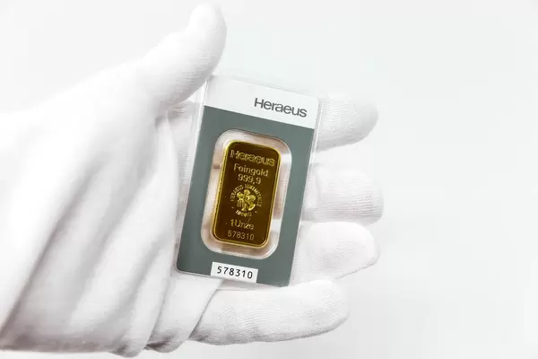 Hand in weißem Handschuh hält einen Heraeus Goldbarren