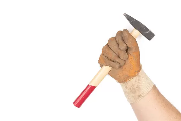 Hand in work gloves with hammer above white background with copy space