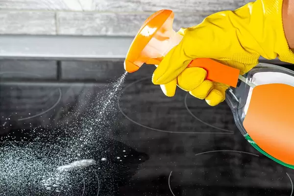 Hand in yellow household gloves with spray to clean the cooking surface
