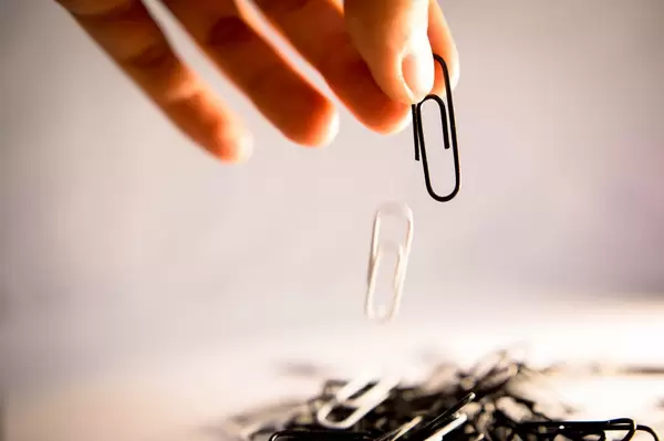 Hand lässt zwei Büroklammern fallen