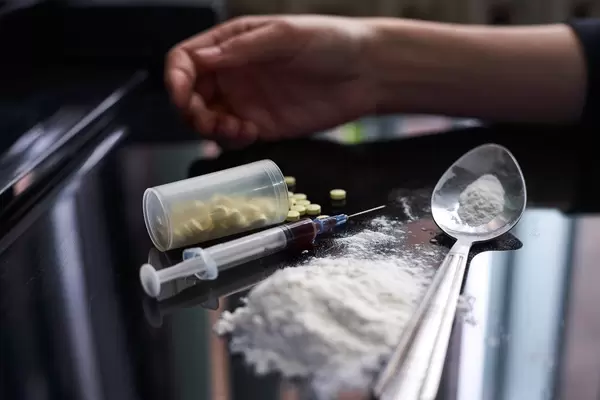 Hand lying near heroin powder, spoon and drug injection syringe