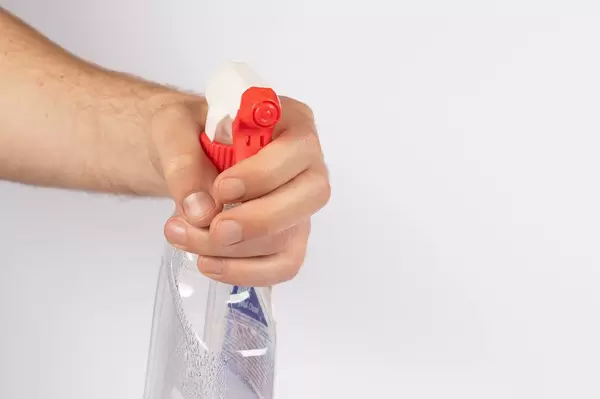 Hand mit einem Putzmittel vor weißem Hintergrund