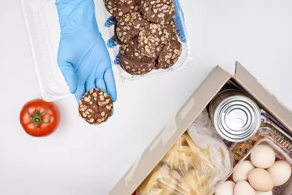 Hand mit Einmalhandschuh serviert Keks aus einem Karton mit Lebensmittelspende wie bei der Tafel