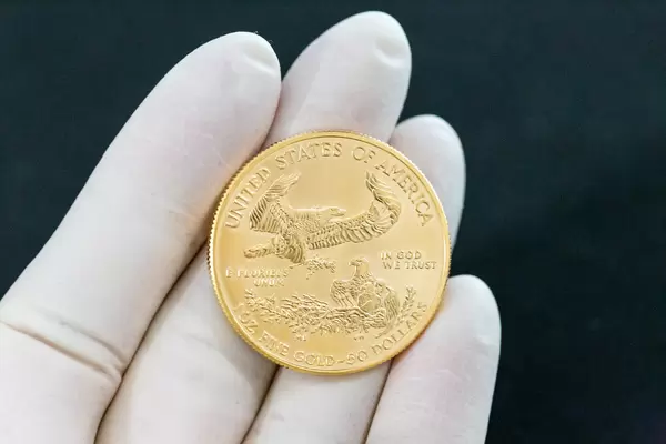 Hand mit Handschuh hält eine goldene 50 US-Dollars American Eagle 2020 Sammlermünze