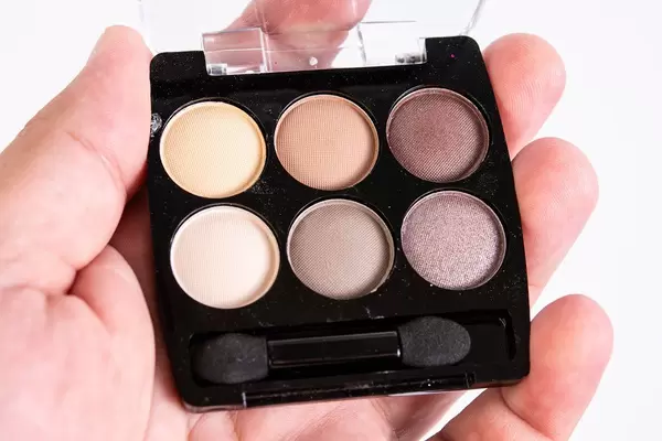 Hand mit Kosmetikdöschen mit sechs Lidschatten in aufeinander abgestimmten Brauntönen vor weiß