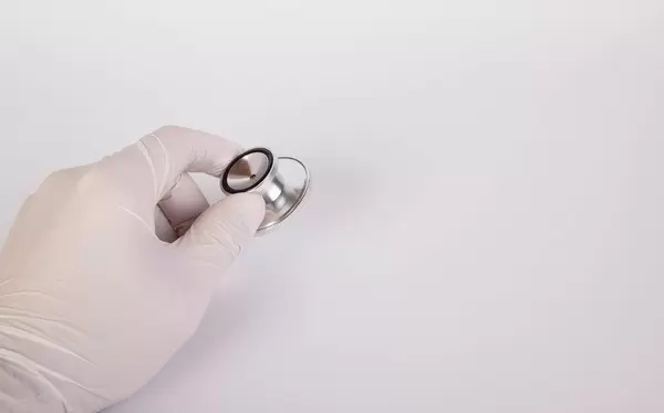 Hand mit Latexhandschuh und Stethoskop, vor weißem Hintergrund