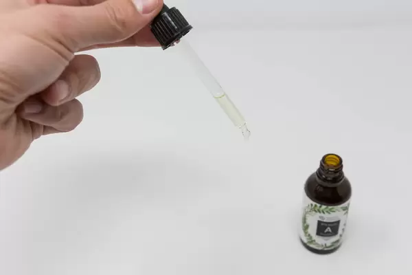 Hand mit Pipette und Vitamin A Tropfen von Natural Elements vor weißem Hintergrund