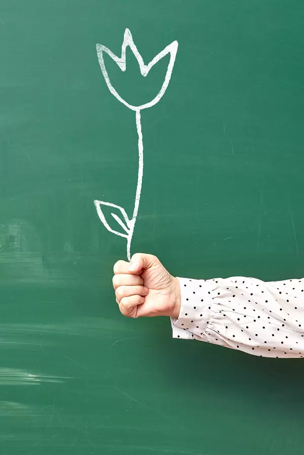 Hand of female holding drawn on the chalkboard flower