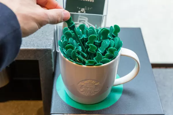Hand picks one stick from a white mug full of green Starbucks coffee stirrers