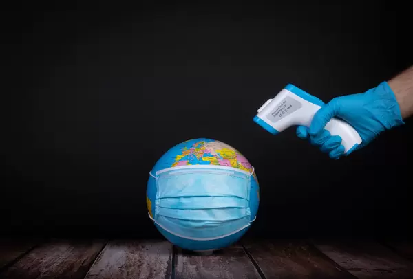 Hand pointing with thermometer at globe with medical face mask