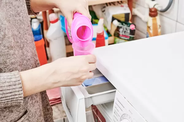 Hand pours liquid detergent into the washing machine