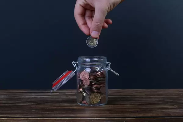 Hand putting coin in money jar